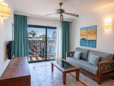 Soggiorno luminoso con mobili in legno, tende turchesi e balcone con vista mare.