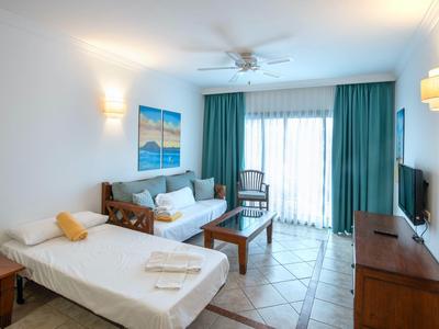 Camera d'hotel luminosa con letto singolo, divano, tavolo e balcone con tende.