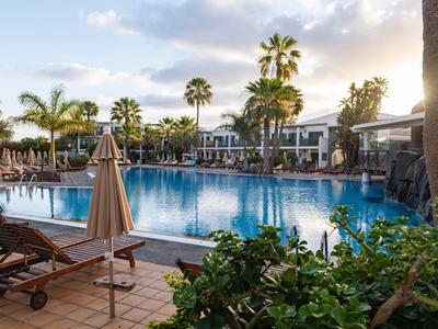 Großer Outdoor-Pool mit Liegestühlen, Sonnenschirmen und Palmen bei Sonnenuntergang.