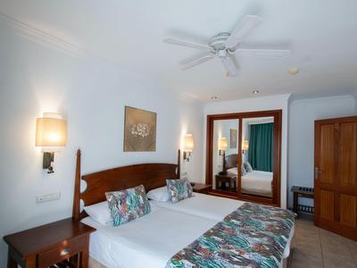 Camera d'hotel luminosa con due letti singoli, biancheria colorata e mobili in legno.