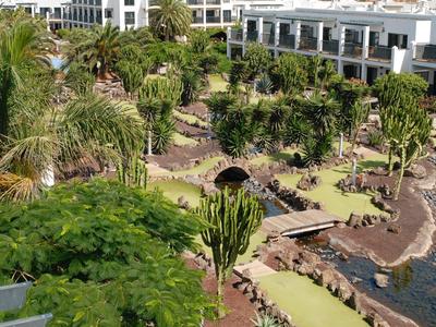 Grüner Hotelgarten mit exotischen Pflanzen, Palmen und Wegen entlang eines felsigen Ufers.
