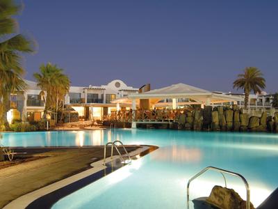 Piscine d'hôtel éclairée avec chaises longues et palmiers au crépuscule.
