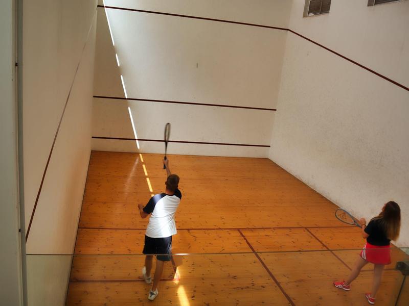 Due bambini giocano a squash in un campo interno luminoso con pavimento in legno.