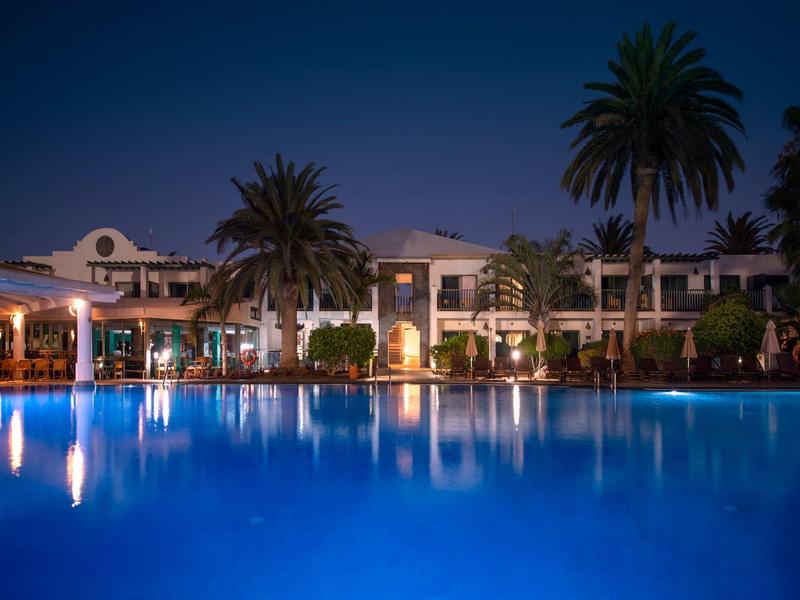 Una piscina dell'hotel illuminata con palme e edifici sullo sfondo di notte.