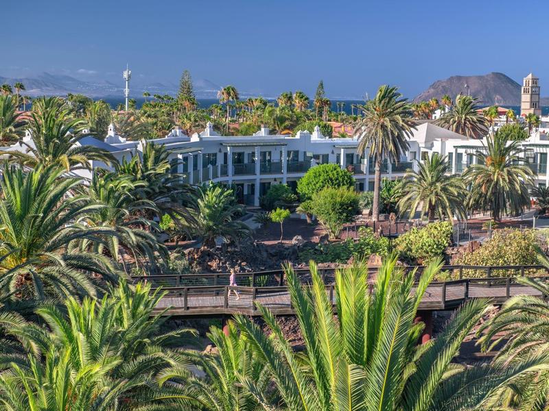 Complesso alberghiero in ambiente tropicale con palme e montagne sullo sfondo.