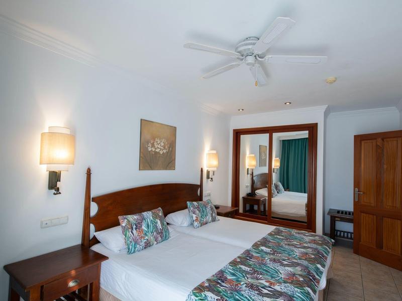 Camera d'hotel luminosa con due letti singoli, biancheria colorata e mobili in legno.