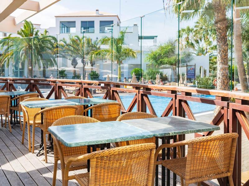 Terrazza con tavoli e sedie in rattan davanti a un hotel con palme.