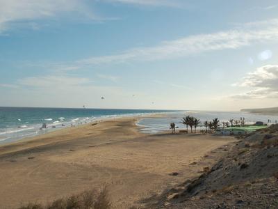 Uitgestrekte zandduin bij de zee met zachte golven en een bewolkte lucht bij zonsondergang.