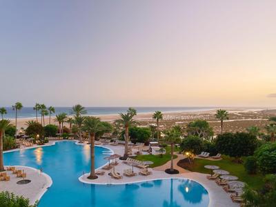 Duży basen z leżakami i palmami obok plaży i morza o zachodzie słońca.