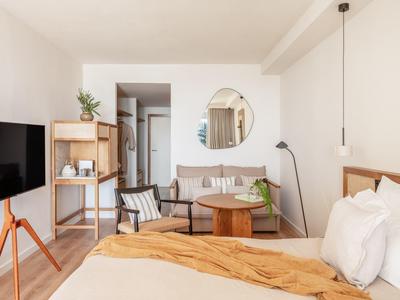 Lichte hotelkamer met tweepersoonsbed, bank, tv en modern interieur.