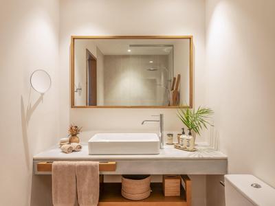 Lichte badkamer met grote spiegel, witte wastafel en handdoekaccenten.