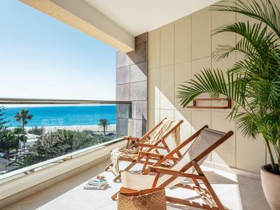 Balkon met drie ligstoelen, planten en uitzicht op zee bij heldere hemel.