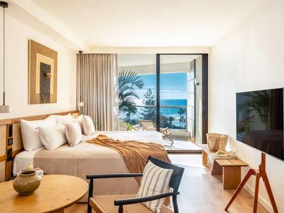 Nowoczesny pokój hotelowy z łóżkiem podwójnym, telewizorem, miejscem do siedzenia i widokiem na morze przez duże okna.