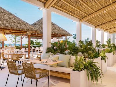 Licht hotelrestaurant met rieten dak en gezellige zithoeken met planten.