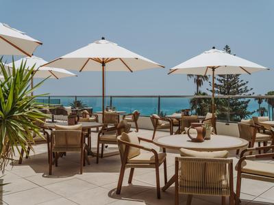 Venkovní restaurace s stoly, židlemi a slunečníky s výhledem na moře.