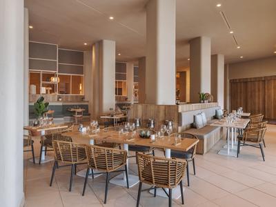 Světlá moderní hotelová restaurace s dřevěnými a ratanovými židlemi a prostřenými stoly.