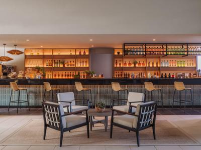 Moderní hotelový bar s dřevěnými regály a pohodlným posezením.