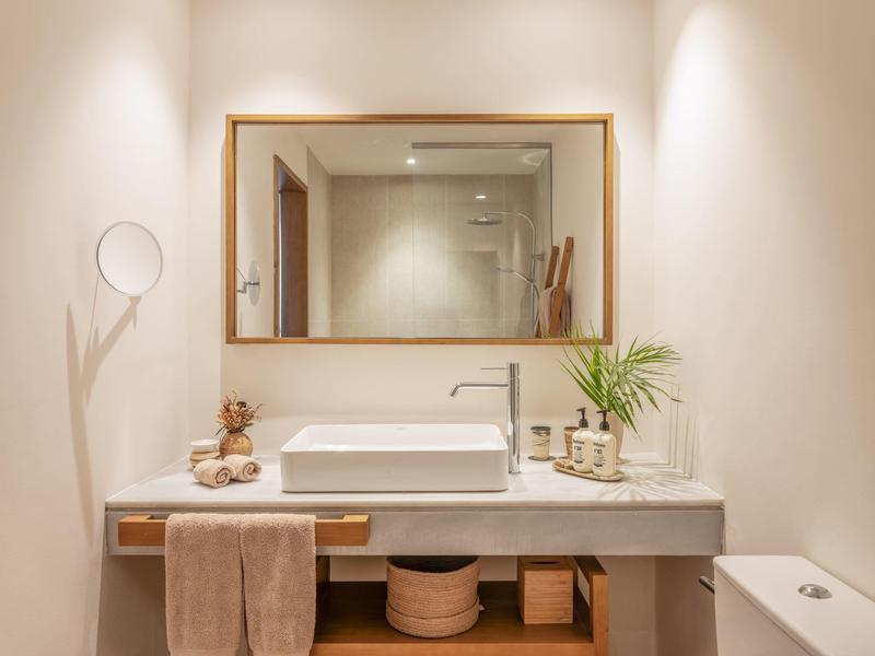 Lichte badkamer met grote spiegel, witte wastafel en handdoekaccenten.