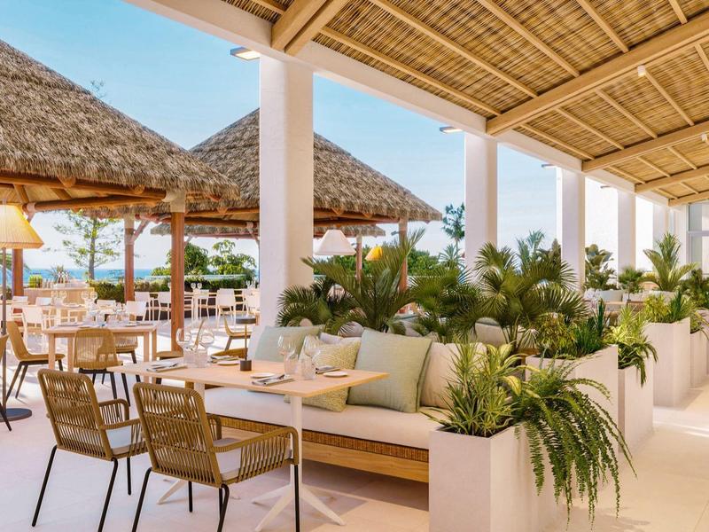 Licht hotelrestaurant met rieten dak en gezellige zithoeken met planten.