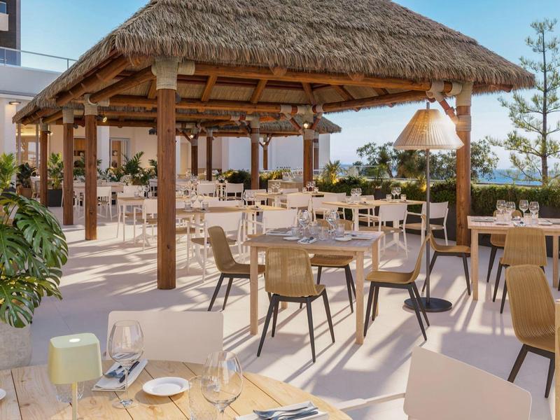 Open restaurantgedeelte met houten dak, stoelen en tafels met uitzicht op zee.