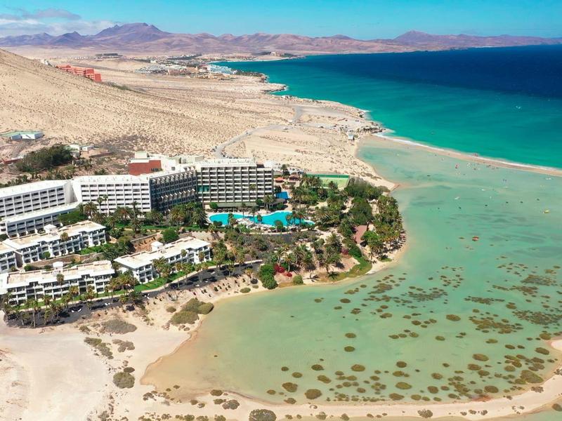 Luxe resort aan het strand met turquoise water en rotsachtige bergen op de achtergrond.