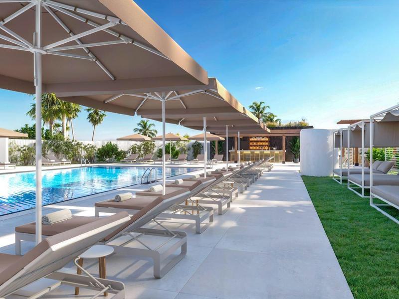 Moderne buitenzwembadruimte met ligstoelen, parasols en groene planten onder een blauwe lucht.