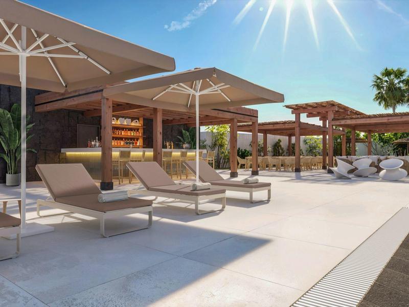 Moderne zwembadomgeving met ligstoelen, parasols en palmbomen onder een zonnige hemel.