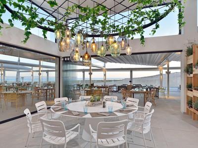 Área exterior moderna de hotel con mesas redondas y sillas blancas bajo un techo de vidrio.