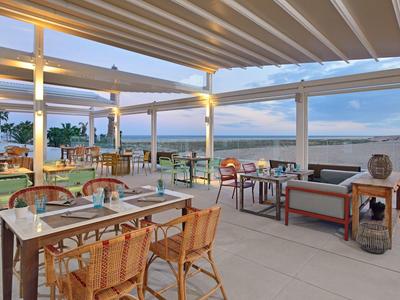Restaurante abierto con sillas y mesas de madera con vista al mar al atardecer.