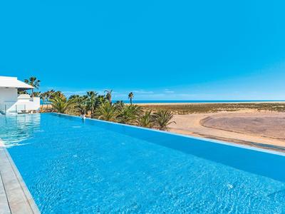 Piscina infinity con vista a la playa, el mar y el cielo azul en un día soleado.