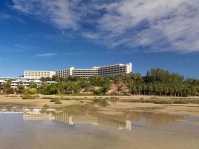 Gran hotel en la playa con cielo despejado y agua reflejante en primer plano.