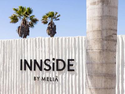Pared blanca con el logo negro de Innside by Meliá y dos palmeras al fondo.