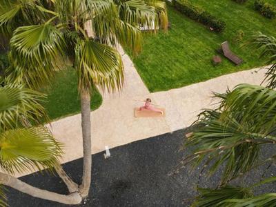 Personne allongée sur une serviette à côté d'une piscine, entourée de palmiers et d'une pelouse verte.