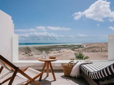 Balcone con sedia e tavolo con vista sulla spiaggia e sul mare sotto un cielo azzurro.