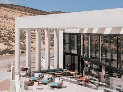 Modernes Außenhotel mit Pool, Sitzbereichen und Blick auf hügelige Landschaft und blauen Himmel.