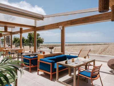 Offener Strandbarbereich mit blauen Sesseln und Aussicht aufs Meer bei klarem Himmel.