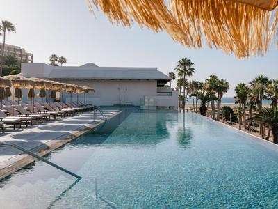 Moderner Infinity-Pool mit Liegestühlen und Palmen unter blauem Himmel.