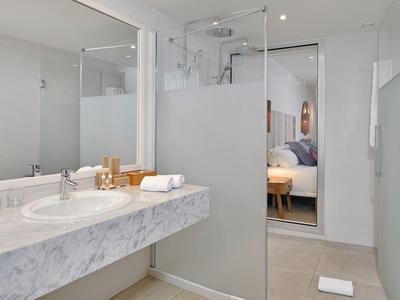 Baño moderno con lavabo de mármol y ducha con mampara de vidrio, vista a una habitación.