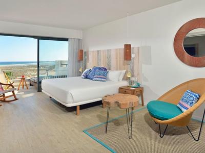 Habitación de hotel moderna con vistas al mar, cama grande, zona de estar y balcón.