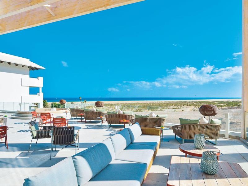 Terraza moderna con asientos cómodos y vista al mar bajo un cielo despejado.