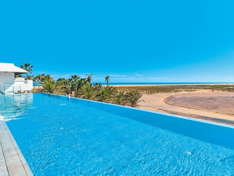 Piscina infinity con vista a la playa, el mar y el cielo azul en un día soleado.
