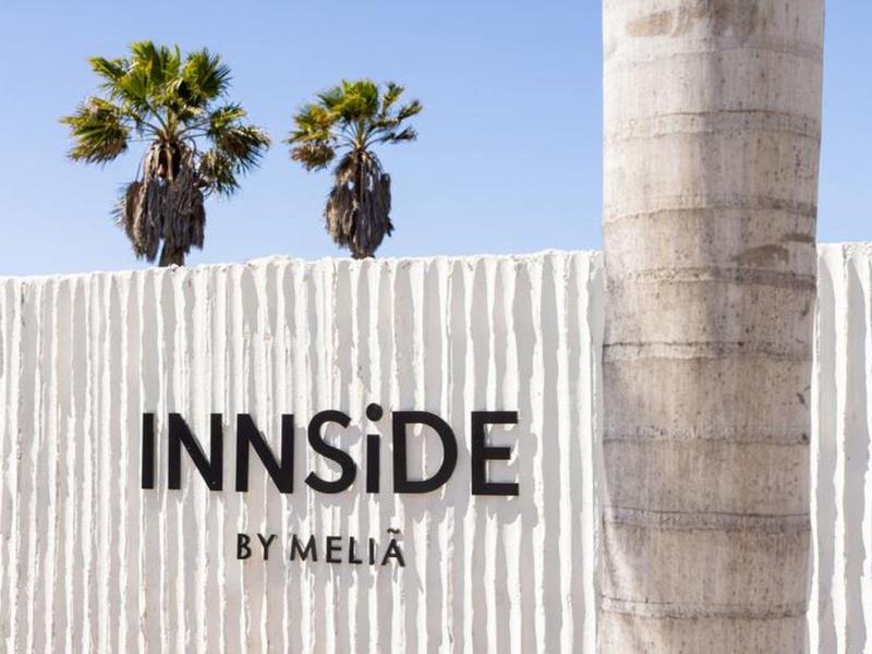 Pared blanca con el logo negro de Innside by Meliá y dos palmeras al fondo.