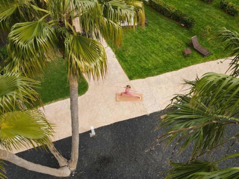 Vista desde arriba de una persona recostada en una acera junto a una piscina bajo palmeras.