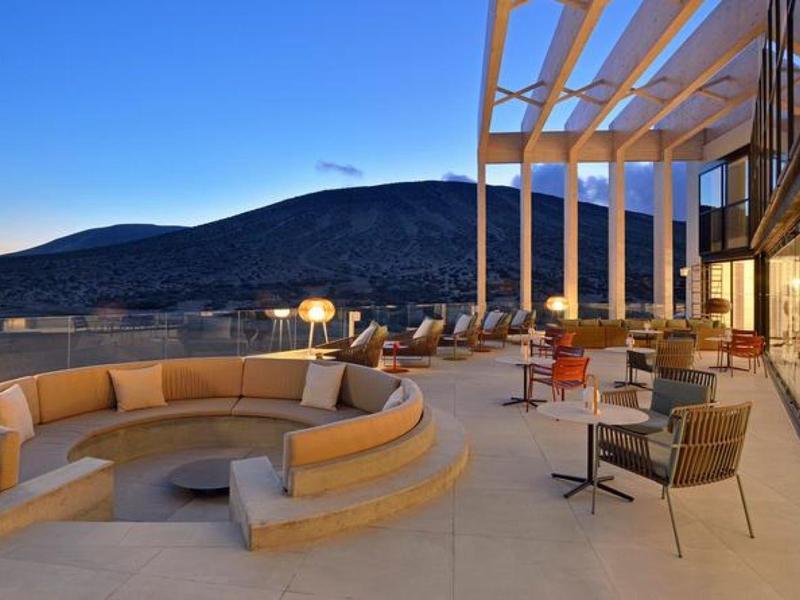 Terraza moderna de hotel con sofás redondos y sillas, rodeada de colinas al atardecer.