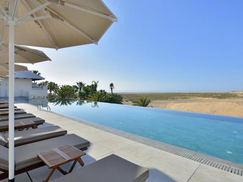 Piscina infinita con tumbonas y sombrillas con vista a un paisaje abierto.
