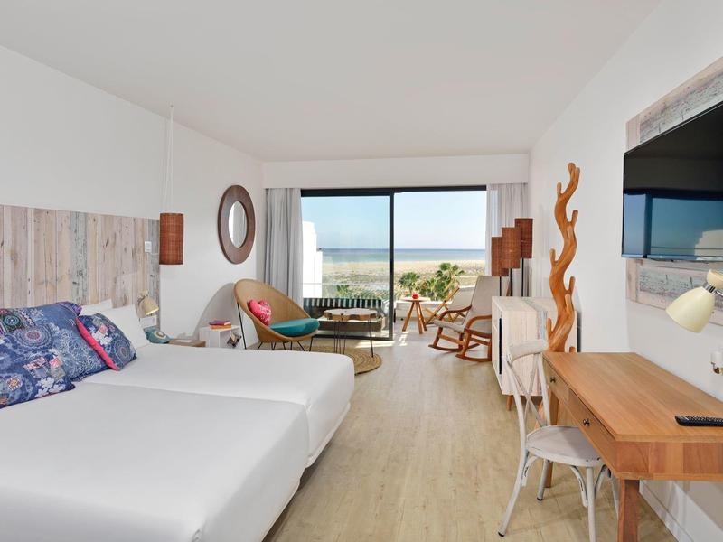 Habitación de hotel moderna con dos camas, muebles de madera y vista al mar a través de ventanas grandes.