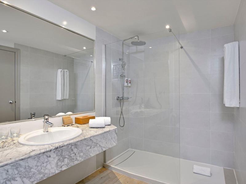 Baño moderno y luminoso con ducha amplia, lavabo y toallas en el hotel.