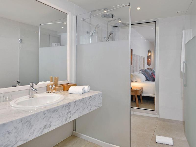 Baño moderno con lavabo de mármol y ducha con mampara de vidrio, vista a una habitación.