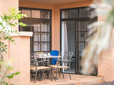 Terrace with table and chairs outside a hotel room with balcony doors.