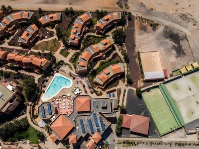 Aerial view of a resort with pools and buildings next to a sandy area.